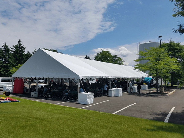 Large white corporate event tent hosting a seated lunch gathering on an asphalt parking lot with guests and decorations.