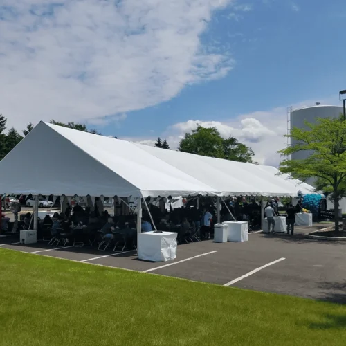 Large white corporate event tent hosting a seated lunch gathering on an asphalt parking lot with guests and decorations.