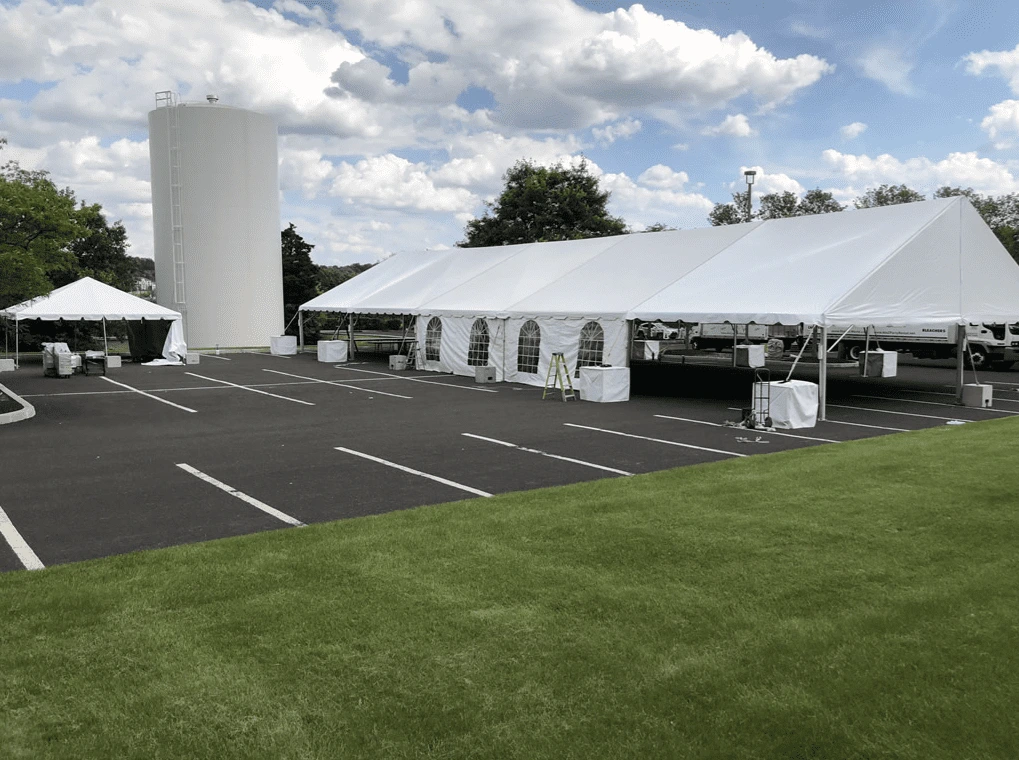 Long white aluminum frame tent setup on an asphalt parking lot featuring sidewalls with arched windows.