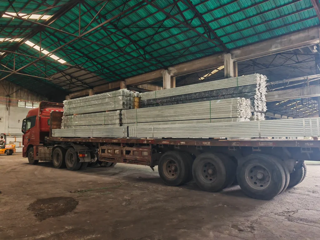 Flatbed truck loaded with wrapped aluminum profiles for clear span tents inside a factory.