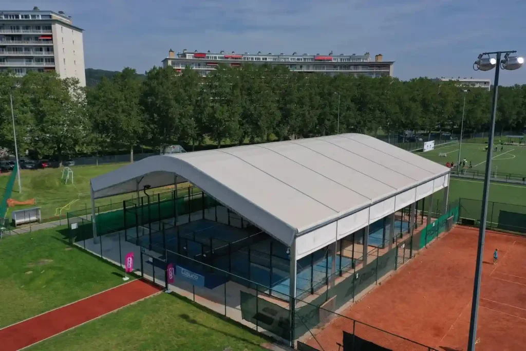 Aerial view of an arch roof clear span tent covering outdoor padel courts at a sports facility.