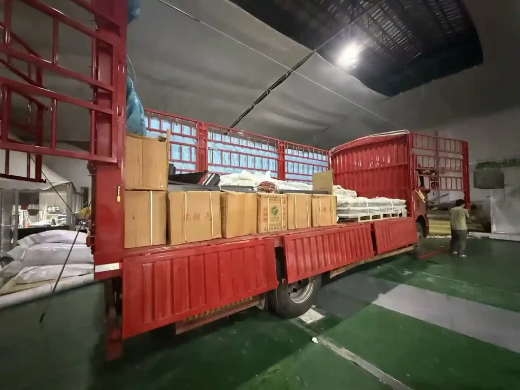 Red truck loaded with cardboard boxes and packaged tent accessories inside a warehouse.