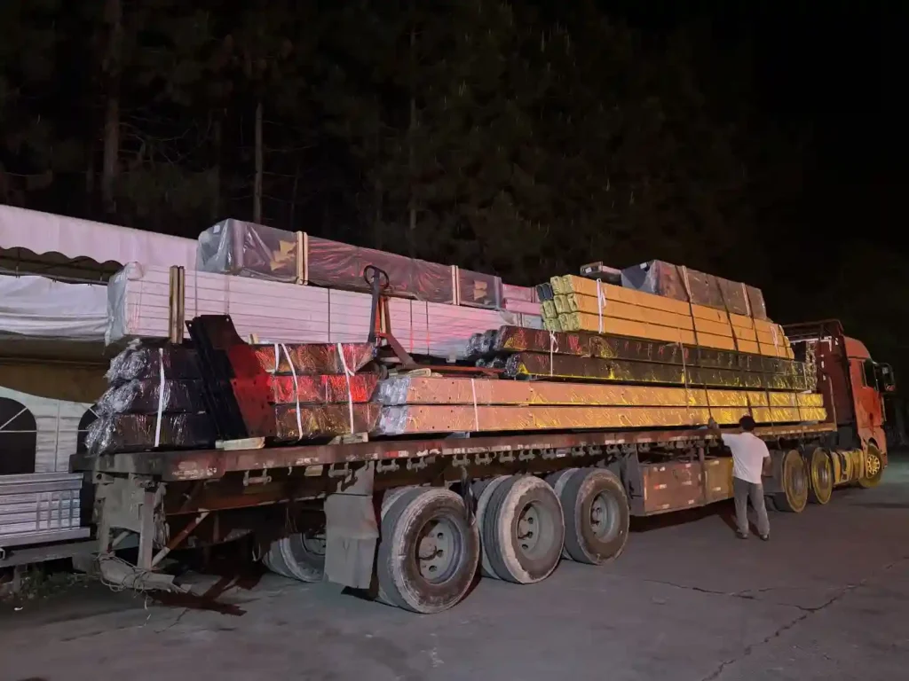 Heavy truck loaded with clear span tent structural beams and parts ready for night transport.