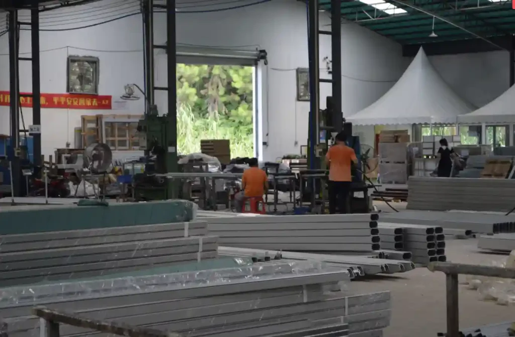 Workers processing aluminum tent components inside a spacious manufacturing facility.