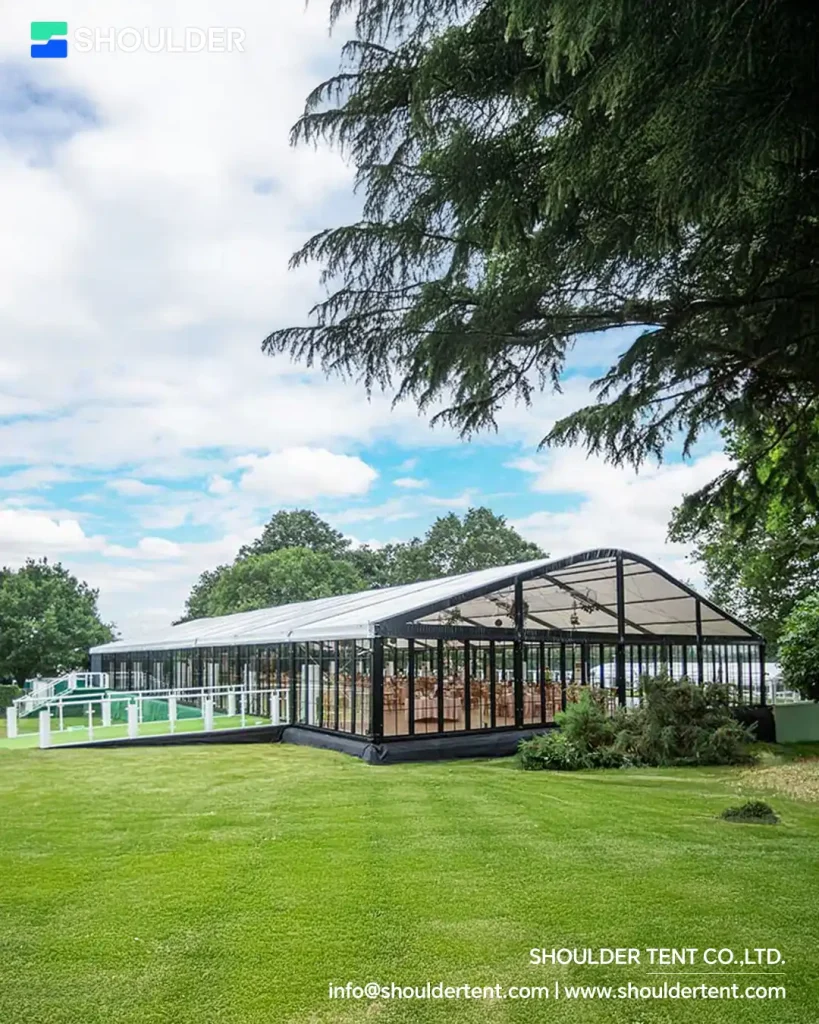 Exterior of a black aluminum frame arcum clear span tent with glass walls on a green lawn.