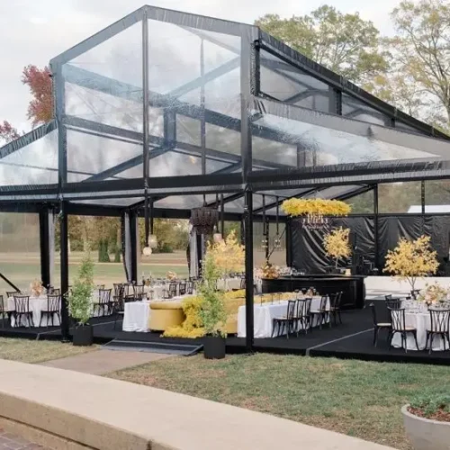 Clear roof raised ridge tent with black aluminum frame, setup for an outdoor banquet.