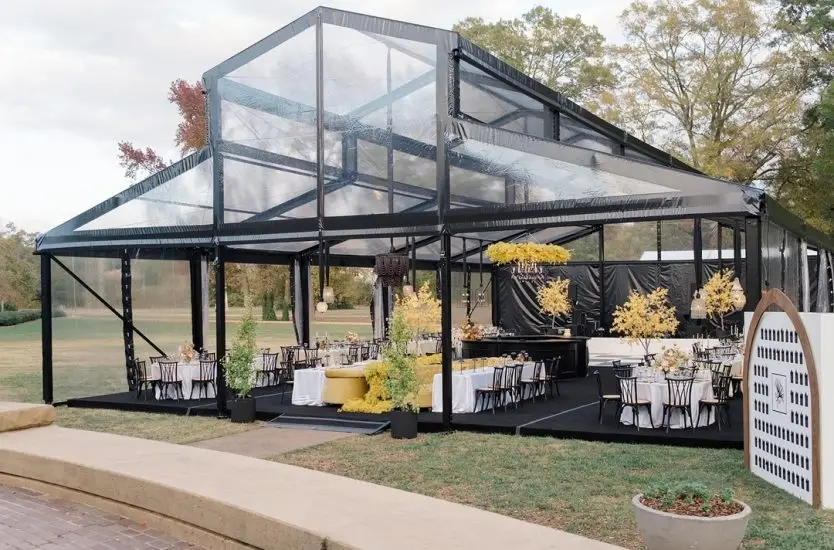 Clear roof raised ridge tent with black aluminum frame, setup for an outdoor banquet.