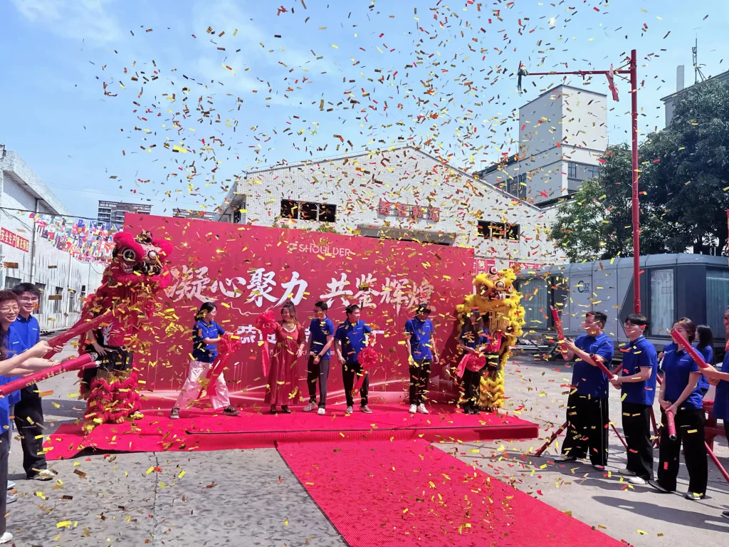 Staff celebrating with confetti and a lion dance at the new Shoulder Tent factory opening.