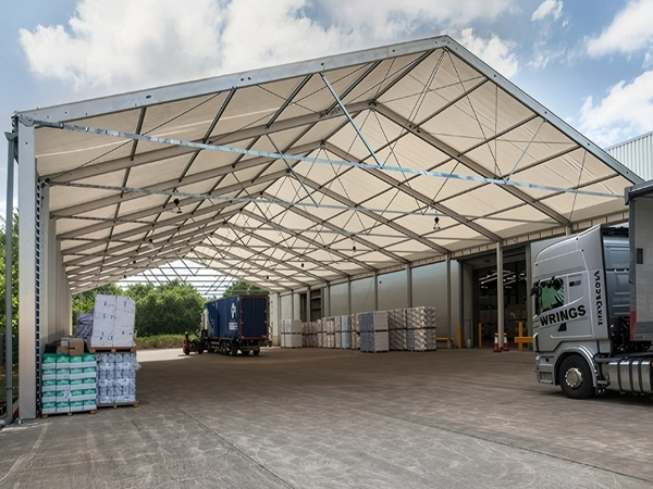 Open-sided clear span aluminum canopy sheltering trucks and cargo at an industrial loading bay.