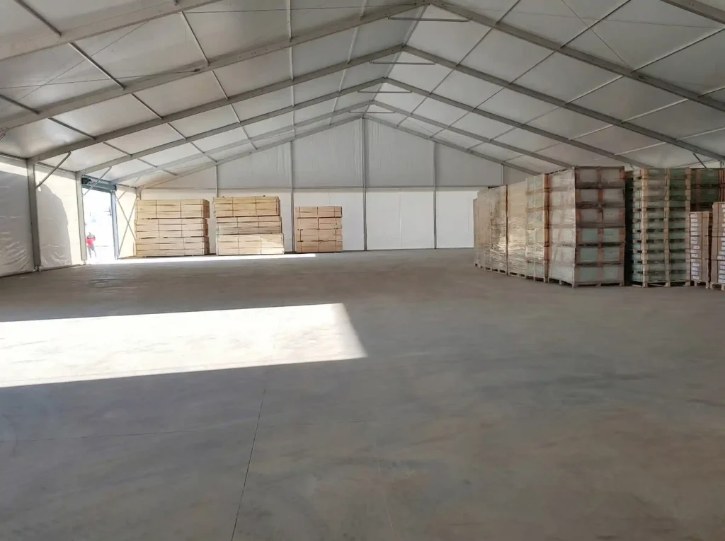 Spacious interior of a clear span warehouse tent storing stacked wood and palletized cargo.
