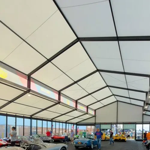 Large clear span exhibition tent with raised roof and glass walls housing a classic car show.