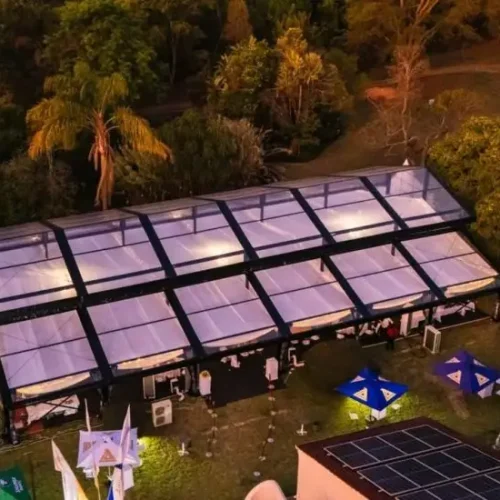 Aerial view of a large raised ridge clear span tent illuminated at night for an event.