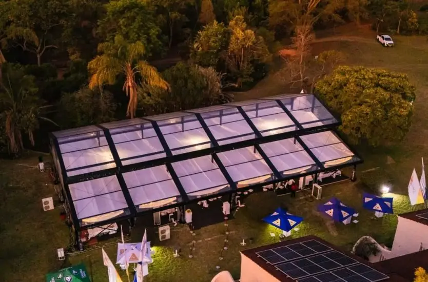 Aerial view of a large raised ridge clear span tent illuminated at night for an event.