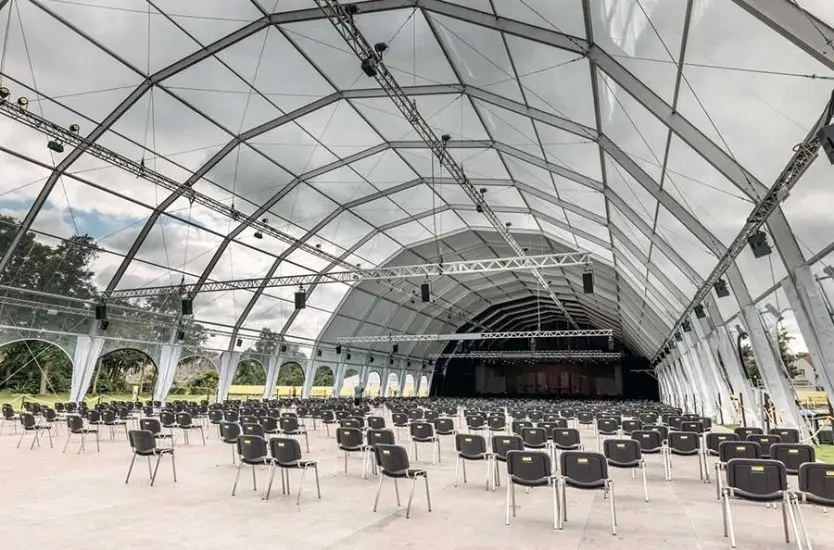 Massive polygonal clear span tent interior with aluminum arches set up for a concert.