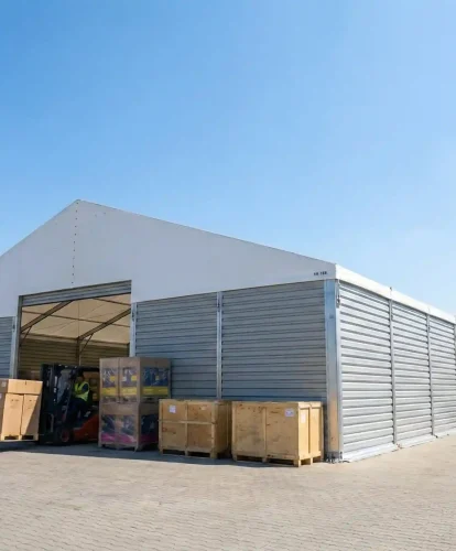 Forklift moving crates outside a modular warehouse tent featuring hard corrugated sidewalls.