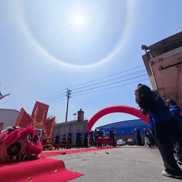 Staff attending the factory opening ceremony outdoors under a bright sun halo