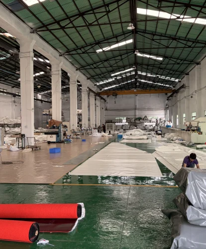 Workers manufacturing large white PVC fabric covers inside a spacious tent production workshop.