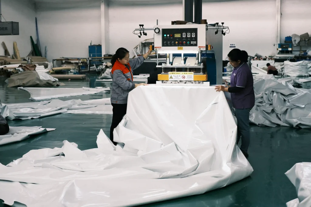 Two factory workers using a machine to weld white PVC fabric for clear span tents.