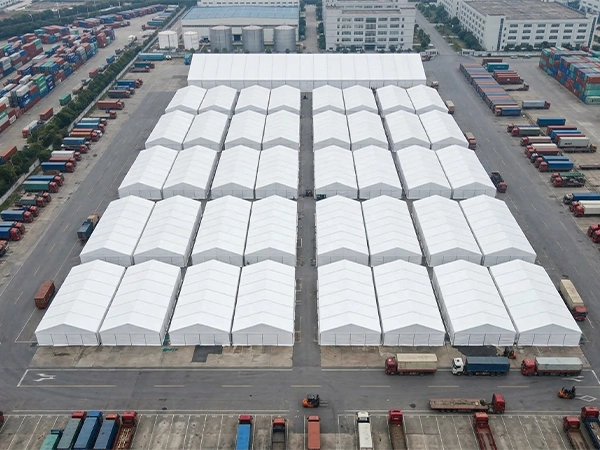 Aerial view of numerous modular white storage tents assembled in a busy container port facility.