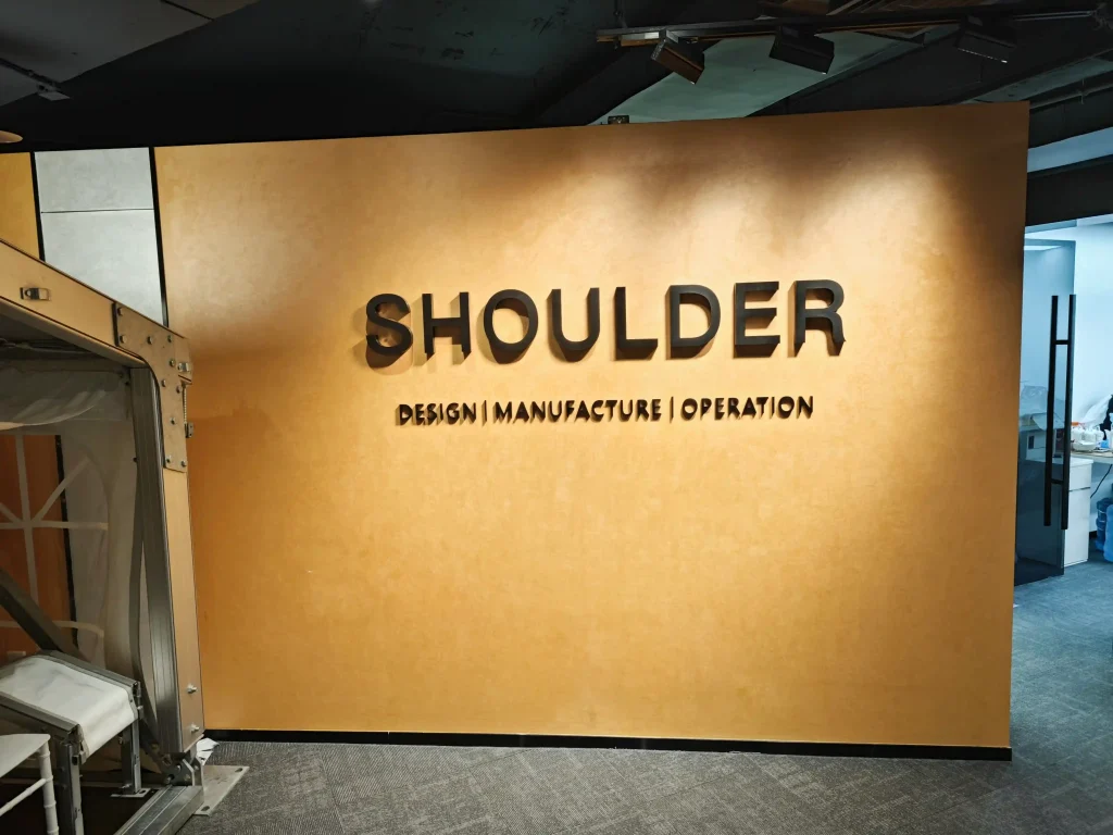 Orange display wall with 3D Shoulder logo next to a small aluminum tent frame sample.