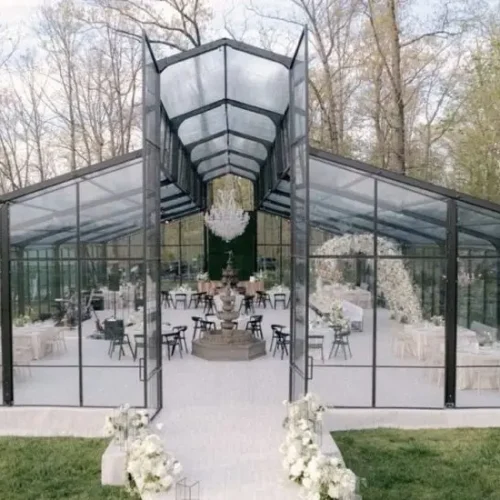 Front entrance of a transparent clear span structure with a high peaked roof and glass panels.