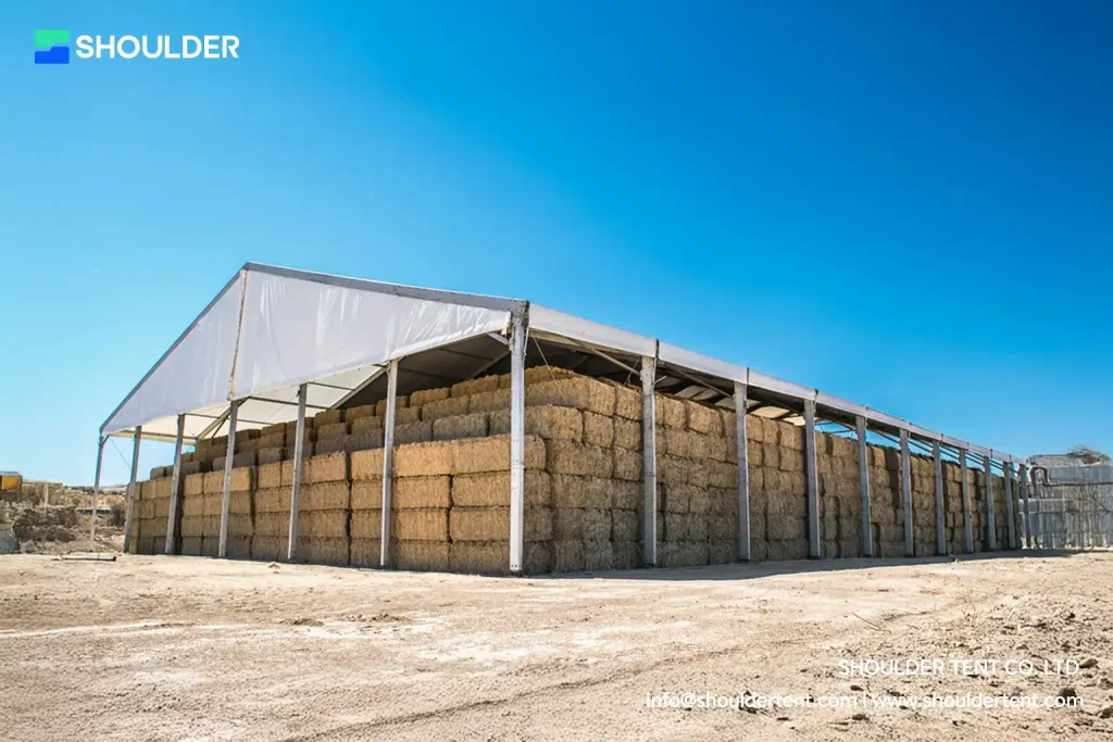 Large aluminum clear span structure utilized for agricultural hay bale storage in an open field.