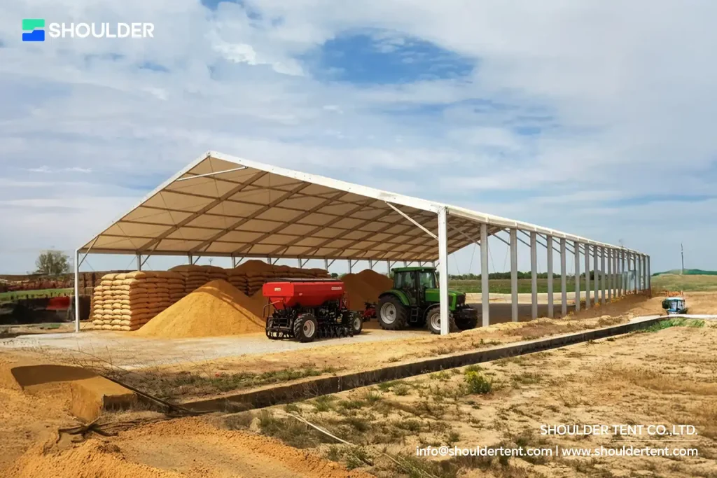 Heavy-duty aluminum clear span canopy sheltering agricultural machinery and harvested crops.
