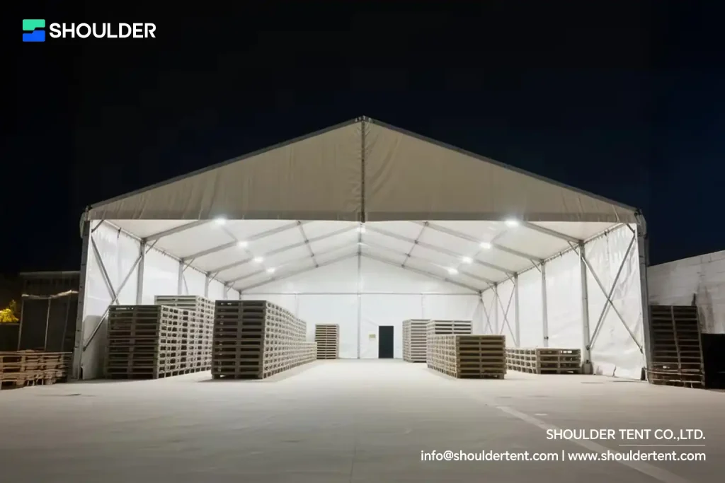 Illuminated interior of a semi-permanent aluminum warehouse structure storing wooden pallets.
