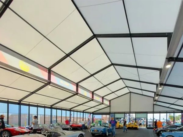 Large clear span exhibition tent with raised roof and glass walls housing a classic car show.