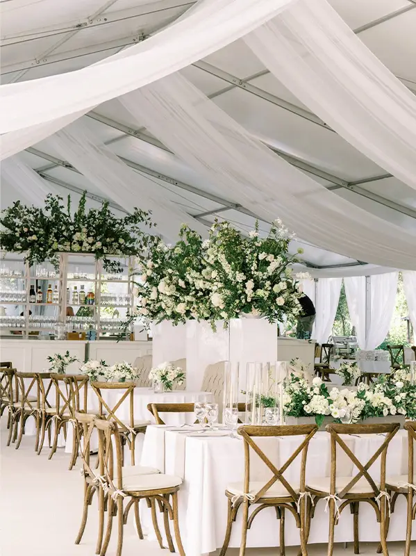 Clear roof event tent interior featuring elegant white fabric draping and dining tables.