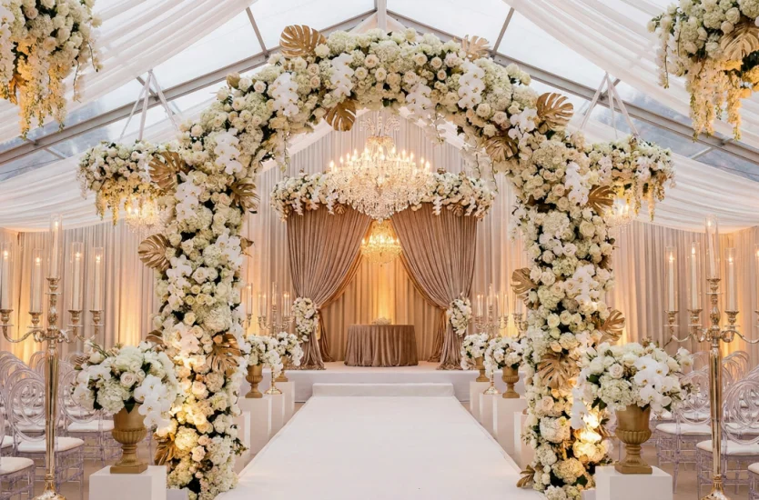 Luxury wedding tent interior featuring a lavish floral arch and clear roof with drapes.