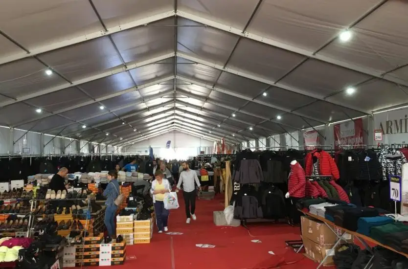 Interior of a clear span commercial tent housing a busy clothing retail outlet with shoppers.