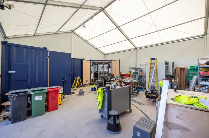 Inside an industrial clear span tent used as a temporary workshop with tools and storage units.