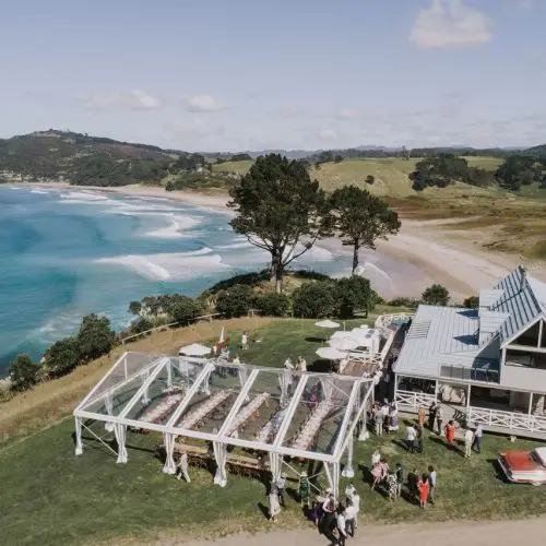 Aerial view of a transparent clear span tent set up on coastal property near the ocean.