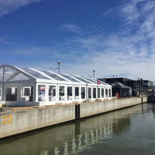 Transparent clear roof event tent installed on a concrete harbor pier next to the water.