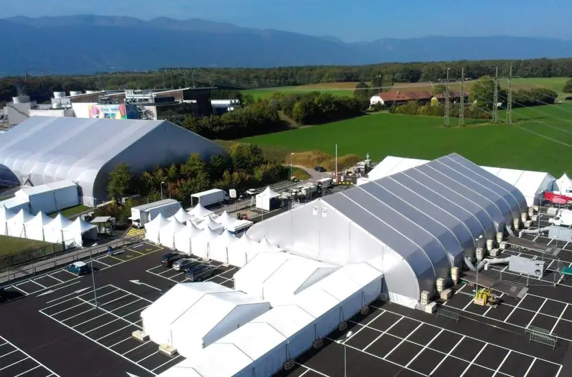 Aerial view of a large white curved roof aluminum tent complex set up in a parking lot.