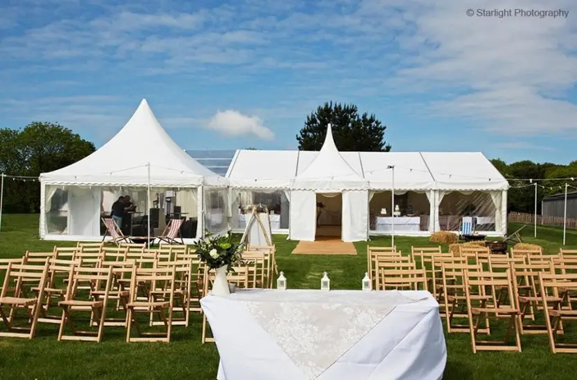 White clear span wedding marquee with a high peak entrance behind ceremony chairs.