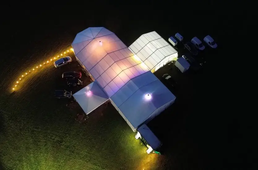 Aerial night view of an illuminated modular clear span tent structure for events.