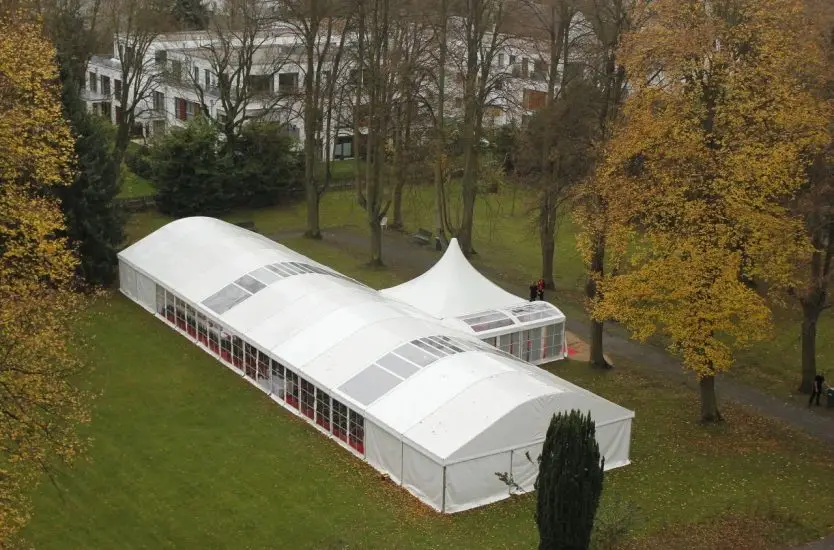 Large white arcum roof clear span tent connected to a pagoda tent in a park.