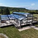 Clear roof event tent with black aluminum frame on a raised deck by a lake.