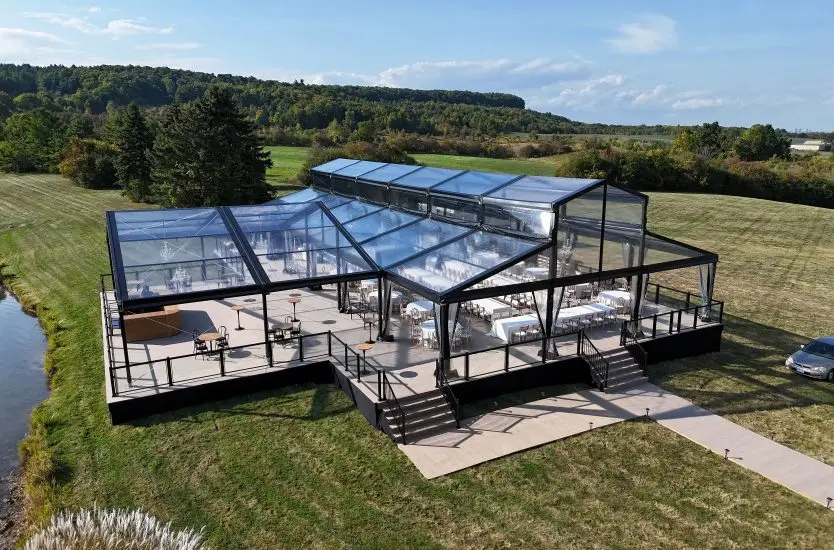 Clear roof event tent with black aluminum frame on a raised deck by a lake.