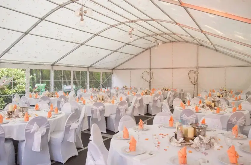 Elegant curved roof wedding tent interior decorated with round tables and white chair covers.