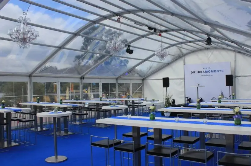 Transparent curved roof clear span tent interior featuring blue flooring and tables for a gala.