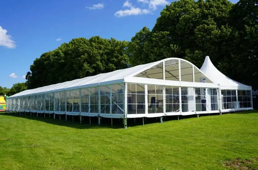 Long white curved roof event tent with clear sidewalls connected to a high peak pagoda tent.