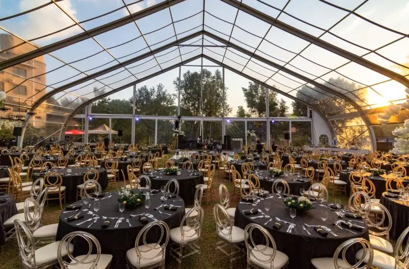 Transparent aluminum event tent interior with round tables set for a sunset wedding banquet.
