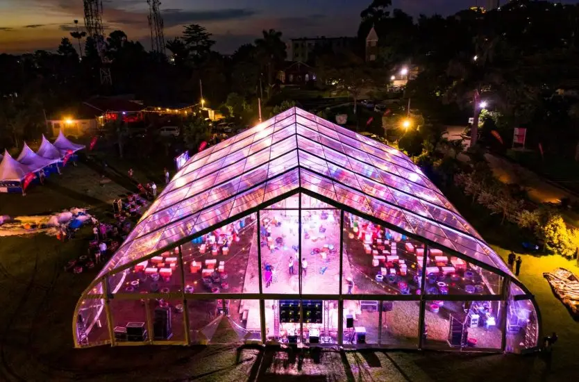 Aerial night view of an illuminated transparent curved roof aluminum tent for a large party.