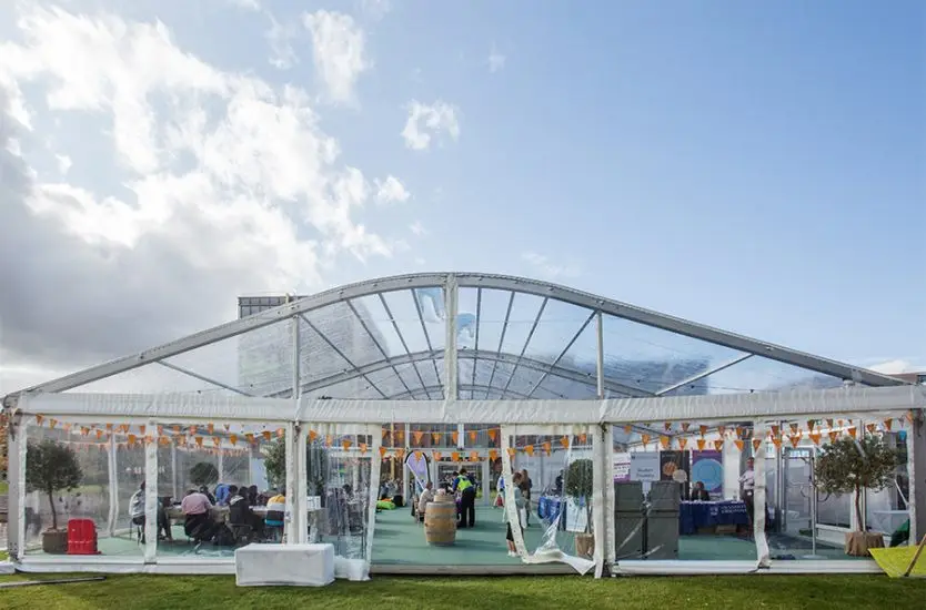 Clear curved roof aluminum tent with transparent walls hosting a public exhibition on the grass.