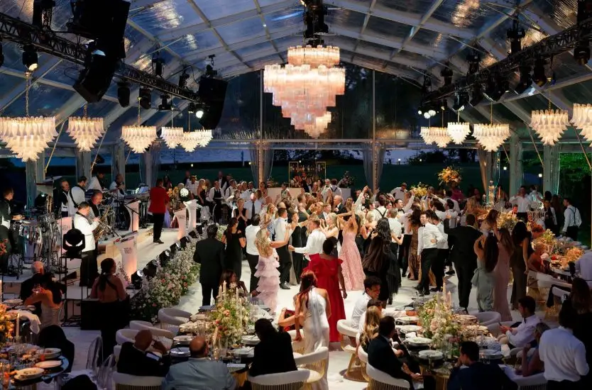 Luxury clear top wedding tent interior at night with chandeliers and dance floor.