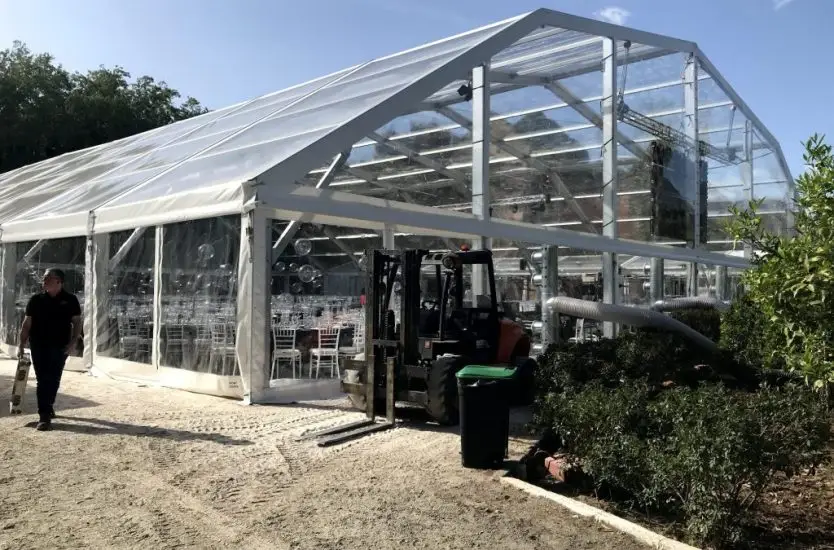 Installation of a clear roof aluminum event tent with a forklift operating outside.