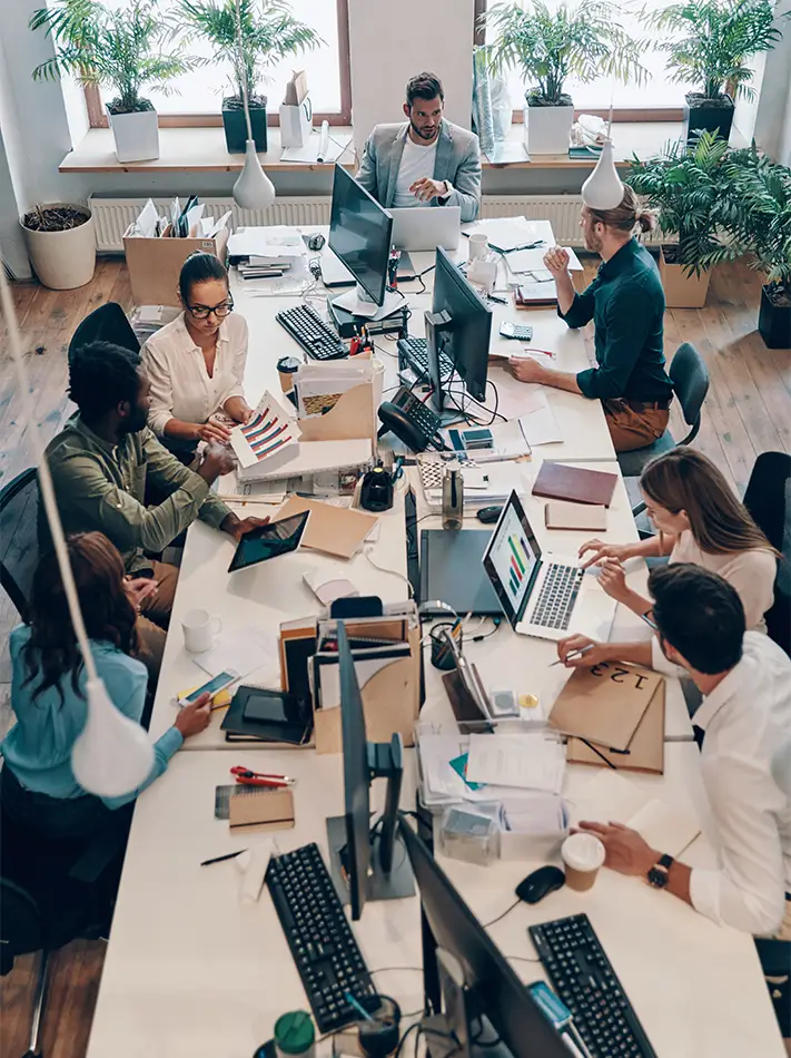 Professional team collaborating around a large office desk with computers and documents.